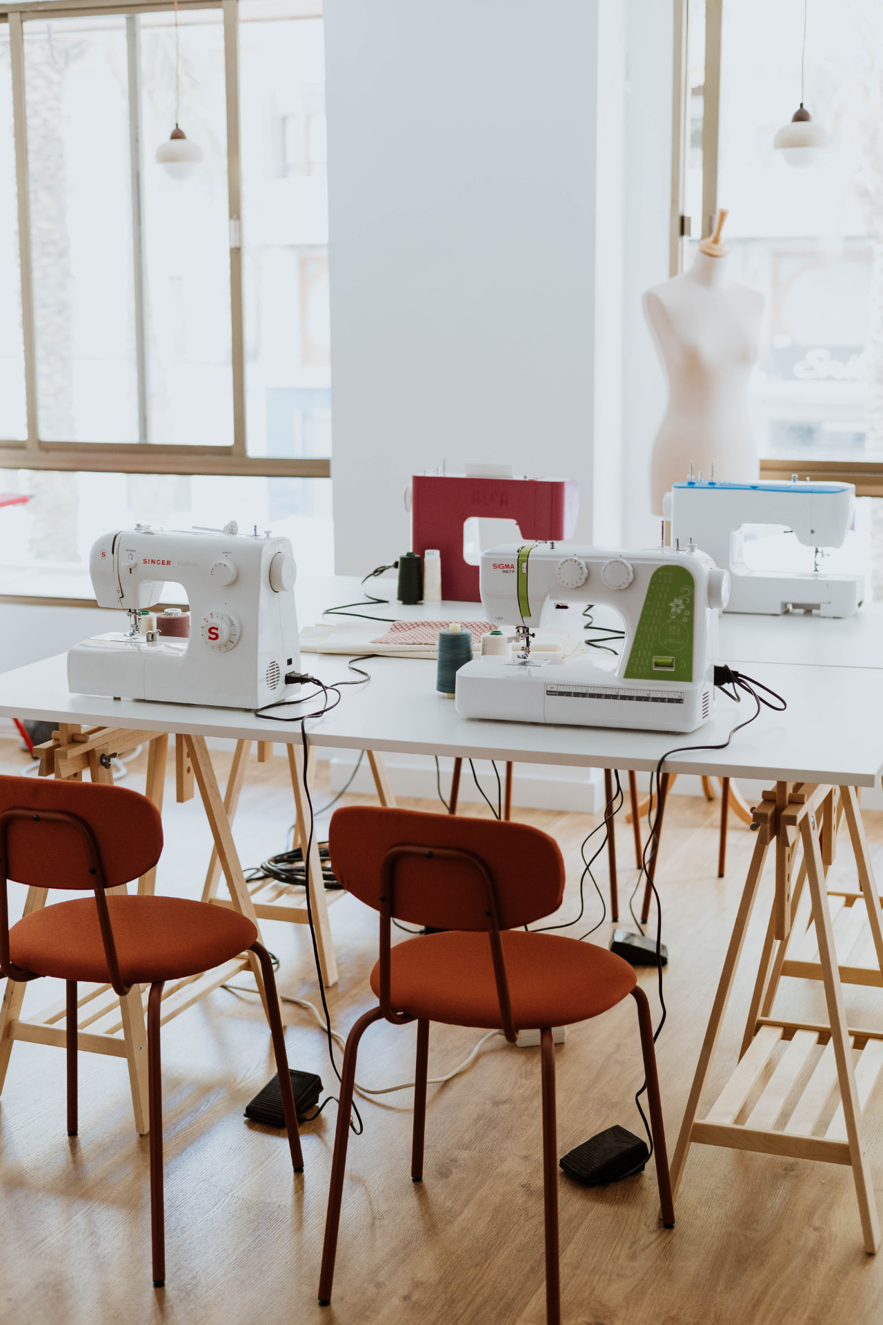 Aula del taller de costura Coser y Cantar en Villena, con máquinas de coser sobre mesas de madera y sillas de color teja