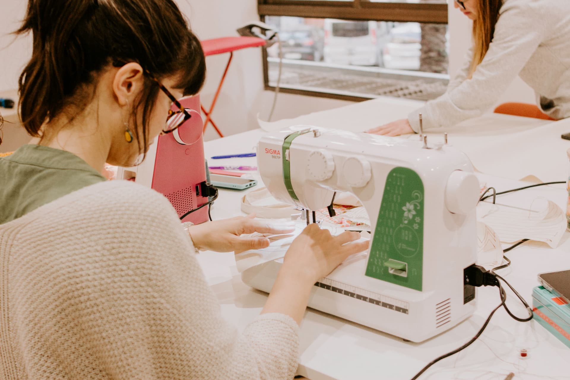 Manos guiando la tela bajo la aguja de una máquina de coser en el taller