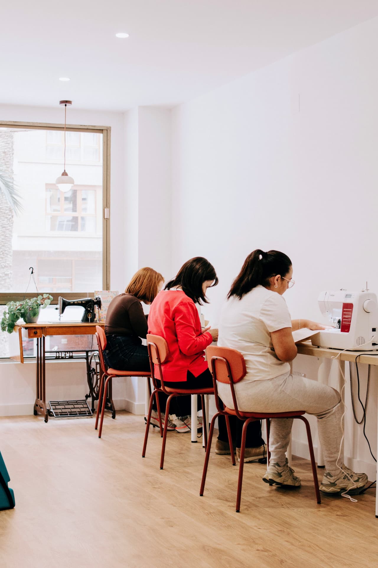 Tres alumnas cosiendo cada una en su máquina, en una de las mesas del taller